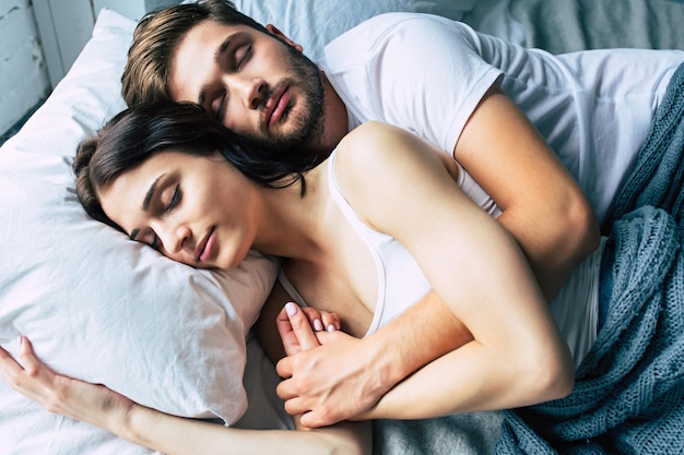 Hermosa pareja joven feliz durmiendo en la cama por la mañana y abrazándose. Concepto de amor y relaciones