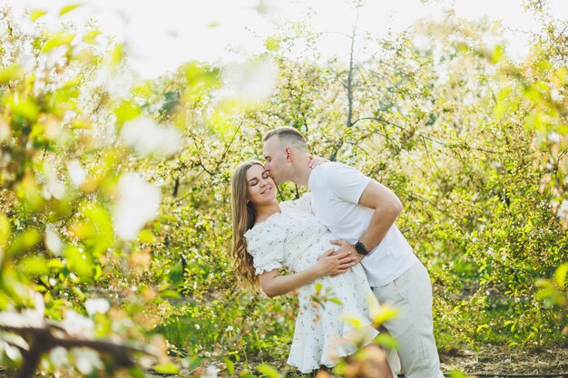 Hermosa pareja joven hombre y mujer embarazada en el jardín de primavera Concepto de familia de estilo de vida de belleza Una madre feliz está esperando un bebé Una pareja joven feliz en un jardín floreciente