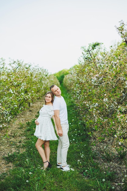 Hermosa pareja joven hombre y mujer embarazada en el jardín de primavera Concepto de familia de estilo de vida de belleza Una madre feliz está esperando un bebé Una pareja joven feliz en un jardín floreciente