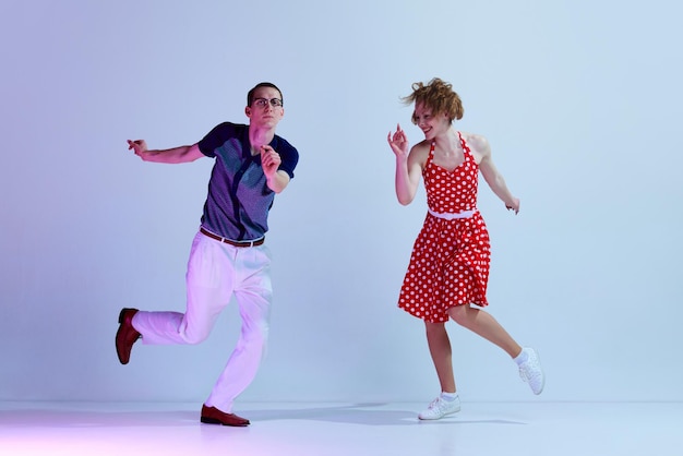 Hermosa pareja joven hombre y mujer en trajes elegantes bailando bailes retro contra azul degradado