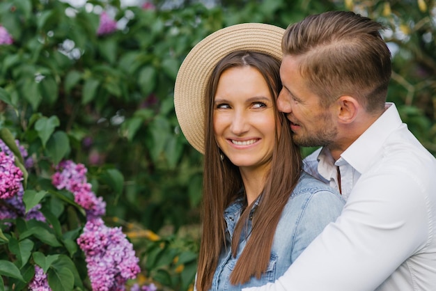 Una hermosa pareja joven en un lugar romántico jardín de lilas en flor de primavera pareja feliz y alegre disfrutando el uno del otro mientras caminan en el jardín