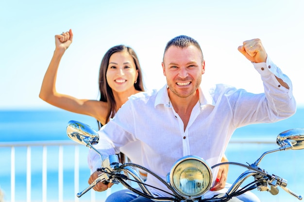 Hermosa pareja joven montando una moto en la playa del paraíso tropical