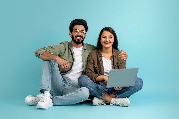 Hermosa pareja joven multicultural que se une en azul usando una computadora portátil