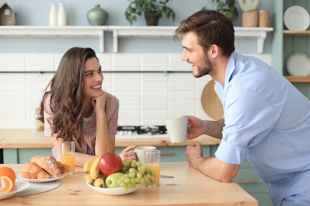 Hermosa pareja joven en pijama se mira y sonríe mientras cocina en la cocina en casa.