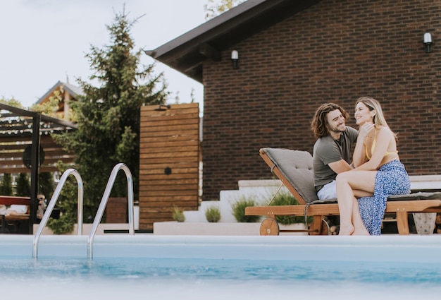 Hermosa pareja joven relajándose junto a la piscina en el patio trasero de la casa