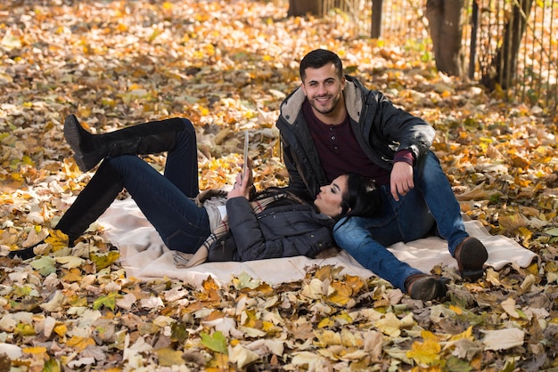 Hermosa pareja joven sentada en el parque en un hermoso día de otoño que están usando Internet a través de una tableta digital