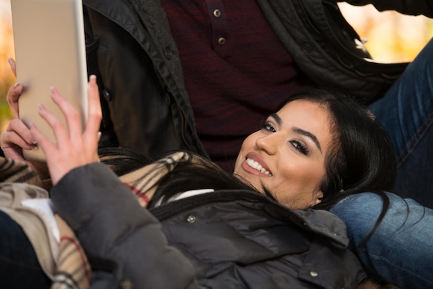 Hermosa pareja joven sentada en el parque en un hermoso día de otoño que están usando Internet a través de una tableta digital