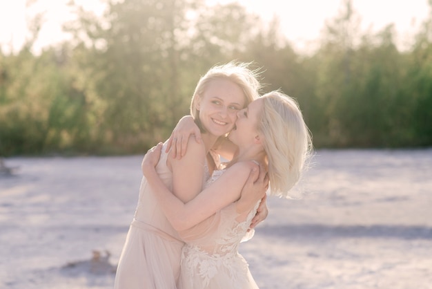 Hermosa pareja de lesbianas caminando sobre la arena a lo largo de la orilla de un río en el día de su boda