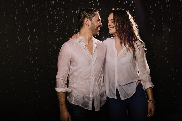 Hermosa pareja bajo la lluvia por la noche, vista romántica, pareja caminando y besándose.