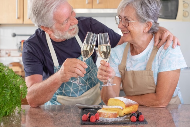 Una hermosa pareja de mayores en la cocina de la casa sosteniendo un vaso de vino listo para comer pastel de ciruela casero