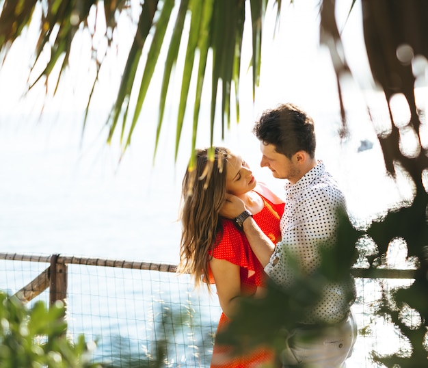 Una hermosa pareja mirando el mar en un día soleado y abrazándose y besándose