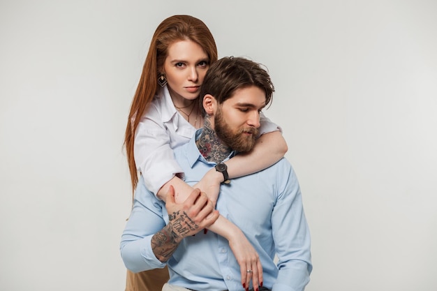 Hermosa pareja de moda brutal hombre hipster y gentil chica bonita pelirroja sobre fondo blanco en el estudio Mujer abrazando a un hombre