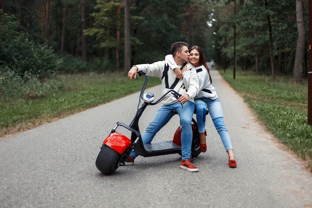 Foto hermosa pareja de moda en ropa de jeans con una bicicleta eléctrica roja en el bosque.