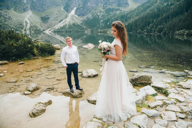 Hermosa pareja moderna cerca de un lago en las montañas hacen fotos de boda