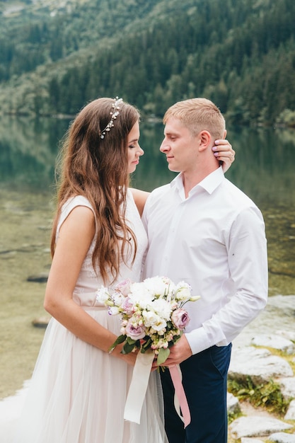 Hermosa pareja moderna cerca de un lago en las montañas hacen fotos de boda