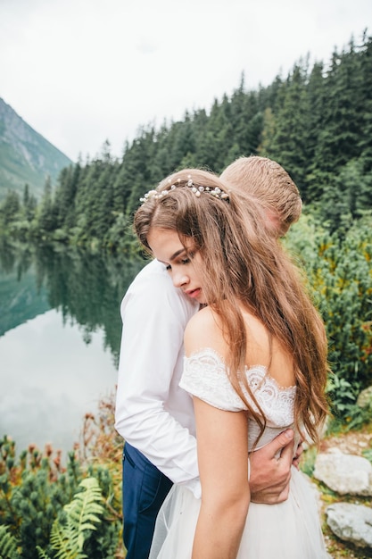 Hermosa pareja moderna cerca de un lago en las montañas hacen fotos de boda