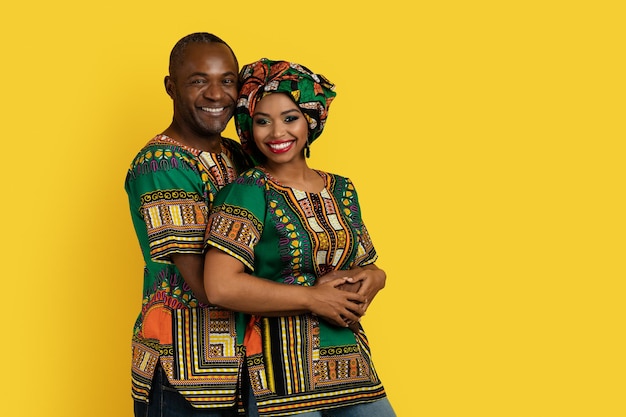 Hermosa pareja negra encantadora en trajes nacionales abrazándose en amarillo