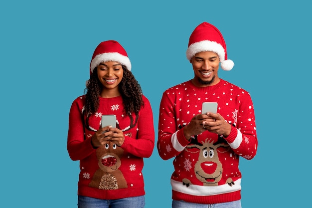 Hermosa pareja negra de Navidad usando teléfonos celulares en azul