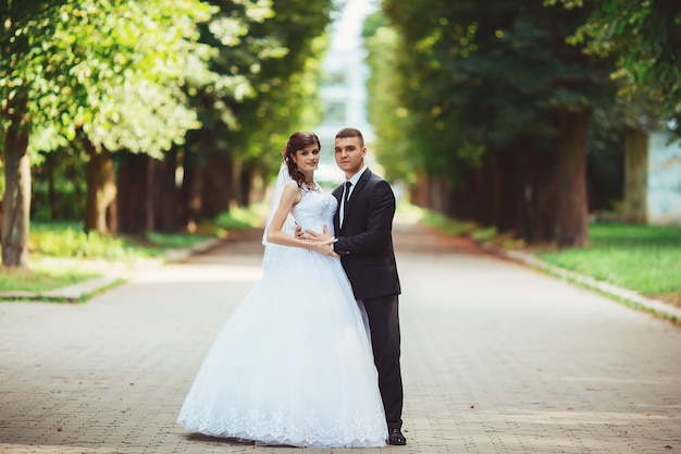 Hermosa pareja de novios. Novia y el novio en el día de la boda caminando al aire libre en primavera la naturaleza. Novios recién casados feliz mujer y hombre abrazando un parque verde.