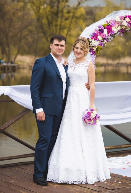 Hermosa pareja de recién casados de pie en el muelle decorado en la ceremonia de la boda