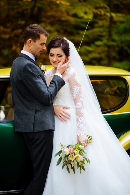 Hermosa pareja de recién casados posando cerca de coche rojo retro