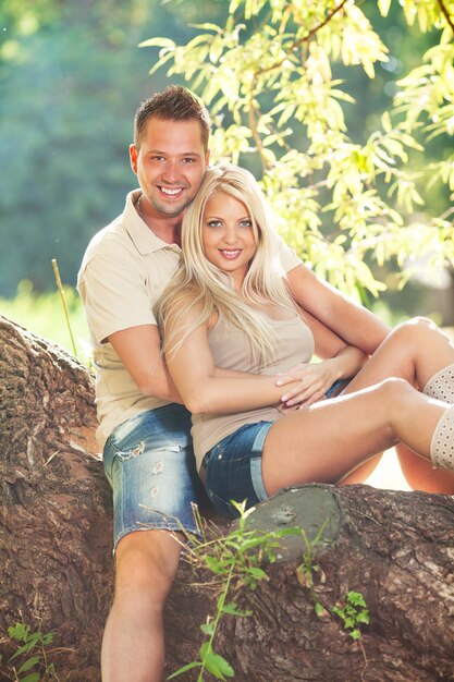 Hermosa pareja romántica abrazada en el parque sentada en el árbol.