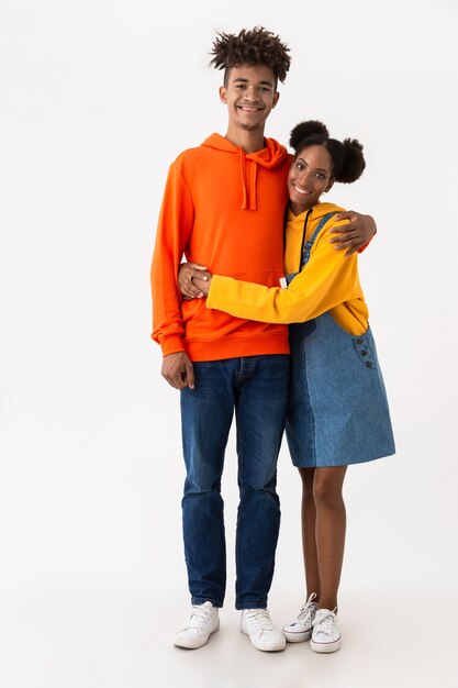 Hermosa pareja en ropa colorida sonriendo mientras está de pie juntos, aislado sobre la pared blanca