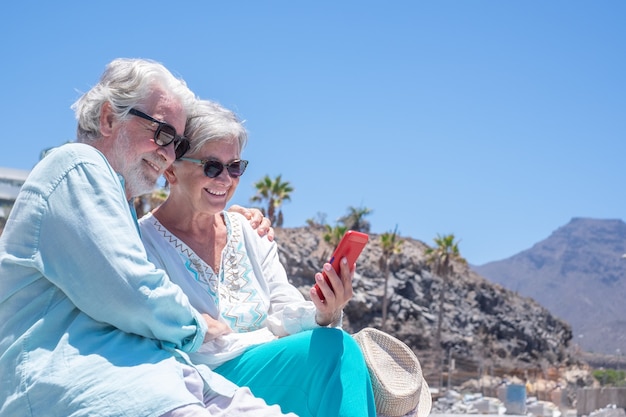 Hermosa pareja senior abrazándose al aire libre mientras usa el teléfono móvil juntos.