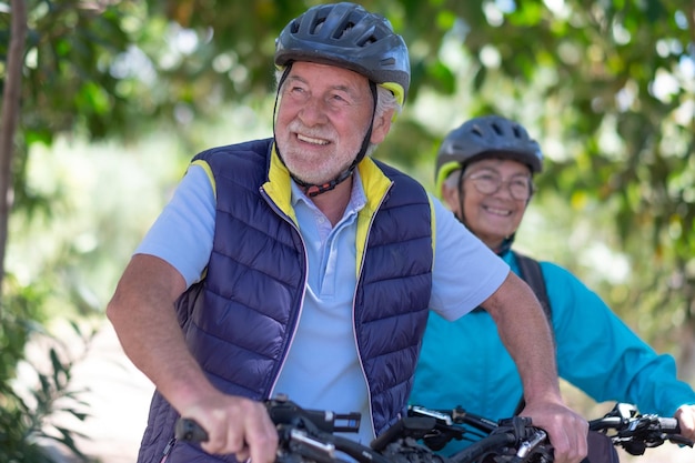 Hermosa pareja senior activa con electrobikes de pie al aire libre en el parque Dos ancianos felices corriendo en la naturaleza con sus bicicletas disfrutando de un estilo de vida saludable