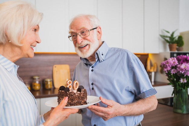 Hermosa pareja senior celebrando el aniversario con pastel de cumpleaños - Pareja de ancianos con fiesta de cumpleaños en casa
