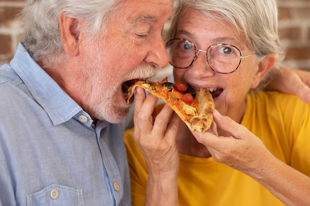 Hermosa pareja senior feliz divirtiéndose juntos comiendo pizza en casa