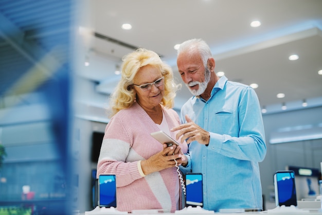 Hermosa pareja senior en tienda de tecnología. Buscando un nuevo teléfono inteligente.