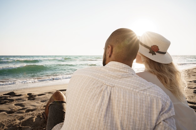 Hermosa pareja sentada en la playa viendo la puesta de sol