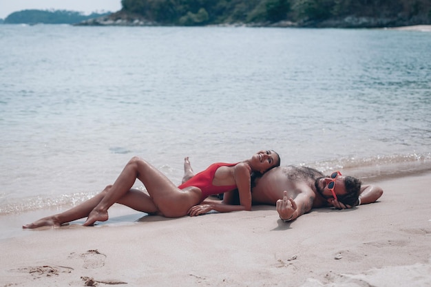 Hermosa pareja sexy chico y chica usando traje de baño cuando está en la playa. Románticamente tumbado en la arena.