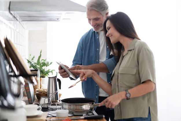 Hermosa pareja usando una tableta digital y sonriendo mientras cocina en la cocina de casa