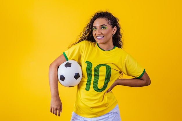 Hermosa partidaria brasileña con una pelota de fútbol en la copa mundial de fondo amarillo 2022