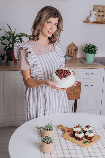 Una hermosa pastelera se para en la cocina y sostiene un plato con postre en sus manos