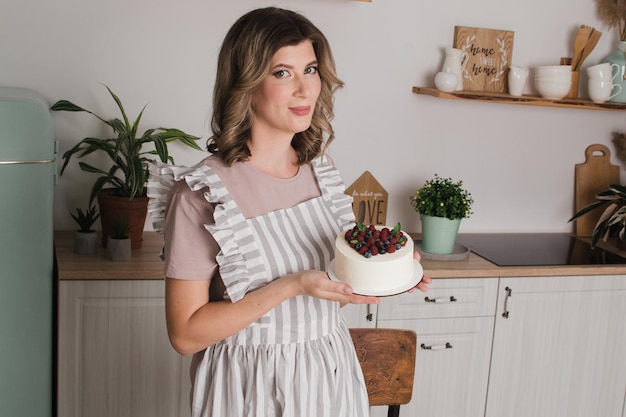 Una hermosa pastelera se para en la cocina y sostiene un plato con postre en sus manos