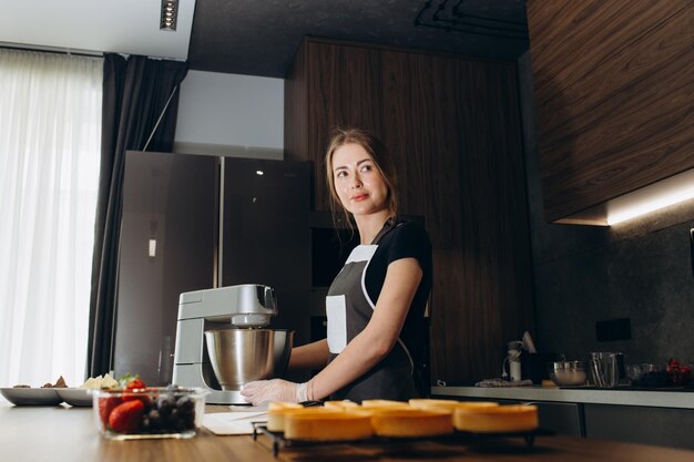 Hermosa pastelera vestida con delantal de pie en la cocina batiendo crema con una batidora