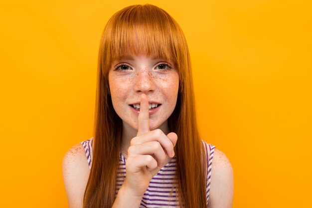 Hermosa pelirroja sostiene un dedo cerca de los labios, silencio