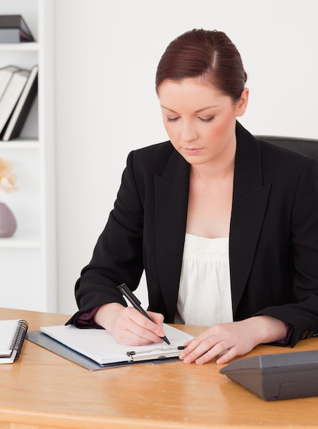 Hermosa pelirroja en traje escribiendo en un bloc de notas