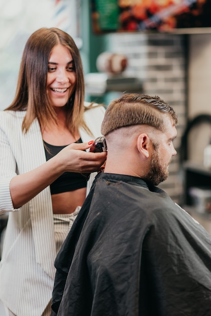 Hermosa peluquera corta a un hombre barbudo en el salón