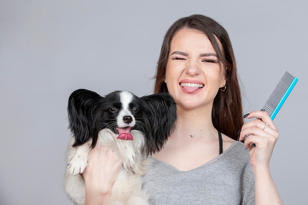 Una hermosa peluquera sostiene a un perro en sus brazos y muestra su lengua Trabajo profesional de una peluquera