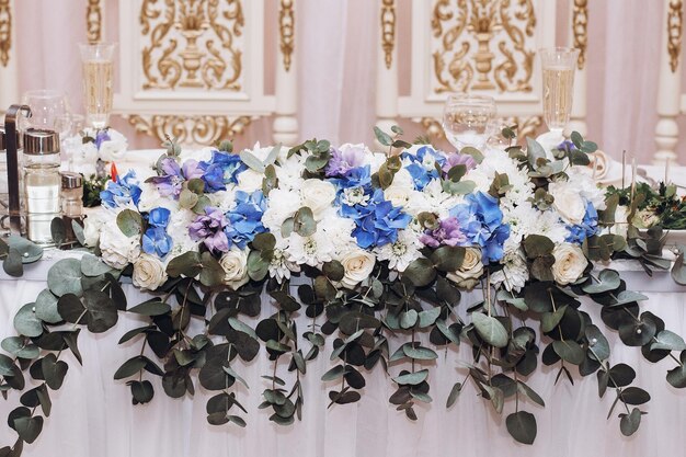 Hermosa pieza central floral en la mesa de la novia y el novio en la recepción de la boda en el restaurante de lujo flores blancas y azules en la mesa blanca cerca del concepto de catering de sillas victorianas doradas