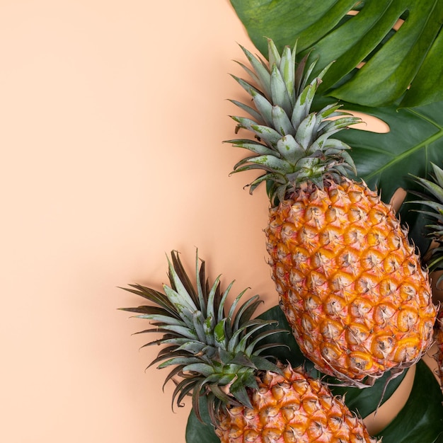 Hermosa piña en hojas de monstera de palmeras tropicales aisladas sobre fondo amarillo naranja pastel brillante vista superior plana sobre la fruta de verano