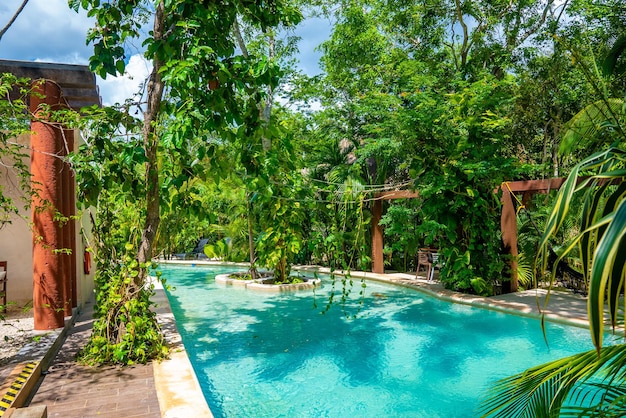 Hermosa piscina en medio de frondosos árboles verdes con columnas arquitectónicas y hamacas en un hotel resort de lujo