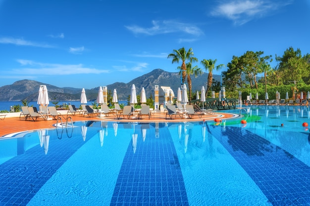 Hermosa piscina con tumbonas y sombrillas al amanecer en verano. Resort de lujo. Liberty hoteles lykia. Oludeniz, Turquía. Paisaje con piscina vacía, tumbonas, árboles verdes, montaña, cielo azul