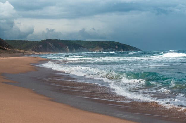 Hermosa playa de arena con grandes rocas en la orilla y en el agua. Poderosas olas en el océano. Salpicaduras de agua del océano en la playa de rocas con acantilados escarpados. Playa de Agva Turquía