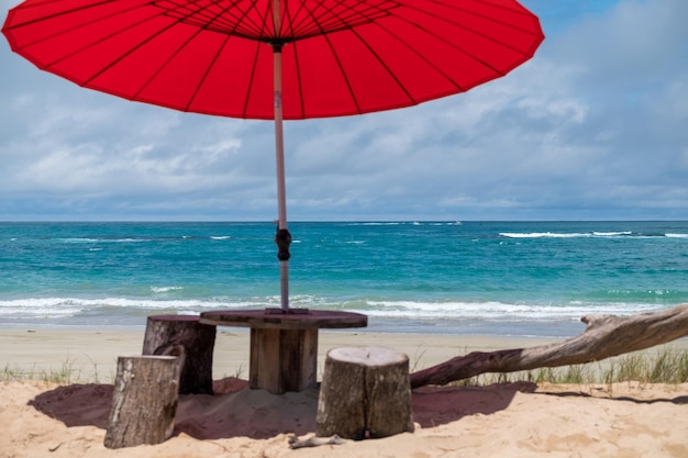 Hermosa playa de color turquesa con una sombrilla roja y un banco en primer plano