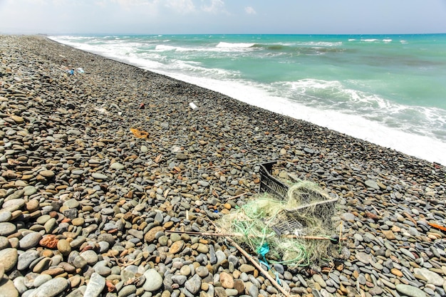 Hermosa playa salvaje de piedras pequeñas y ásperas, estropeada con basura - restos de caja de plástico negra y redes de pesca. Concepto de basura en el medio ambiente oceánico.